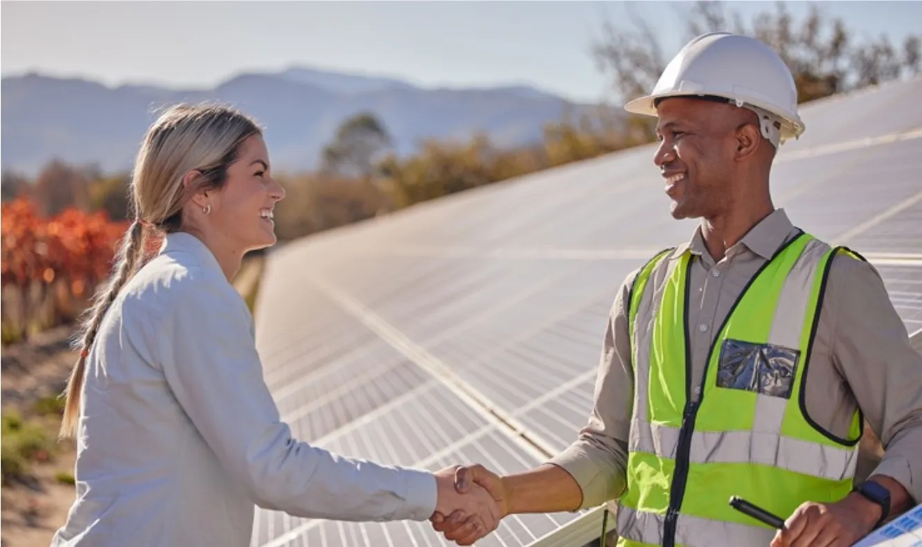 Two people shaking hands infront of solar panels